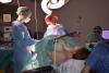 Professionals realitzen una cèsaria a quiròfan. El nadó reposa sobre el pit de mare i el pare, al seu costat, els mira.